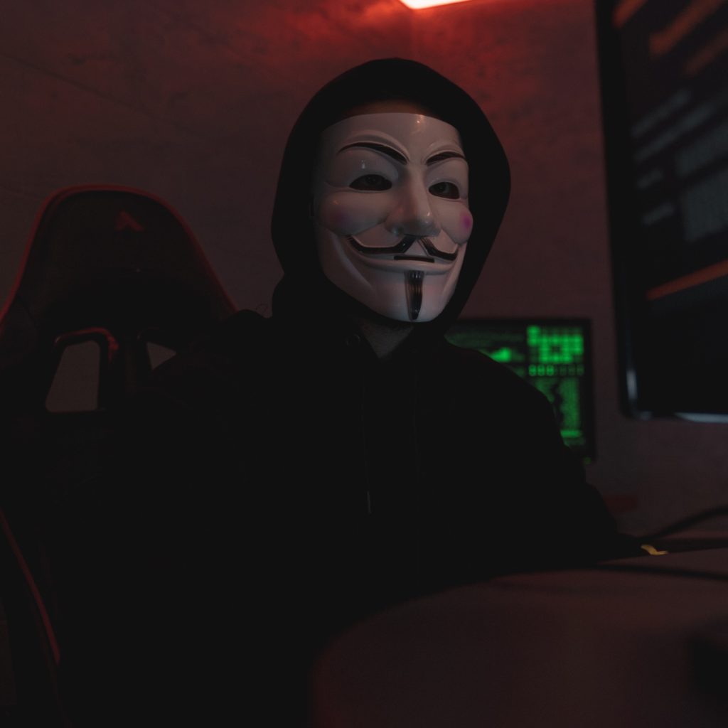 Hacker avec un masque anonymous et une capuche dans le noir.